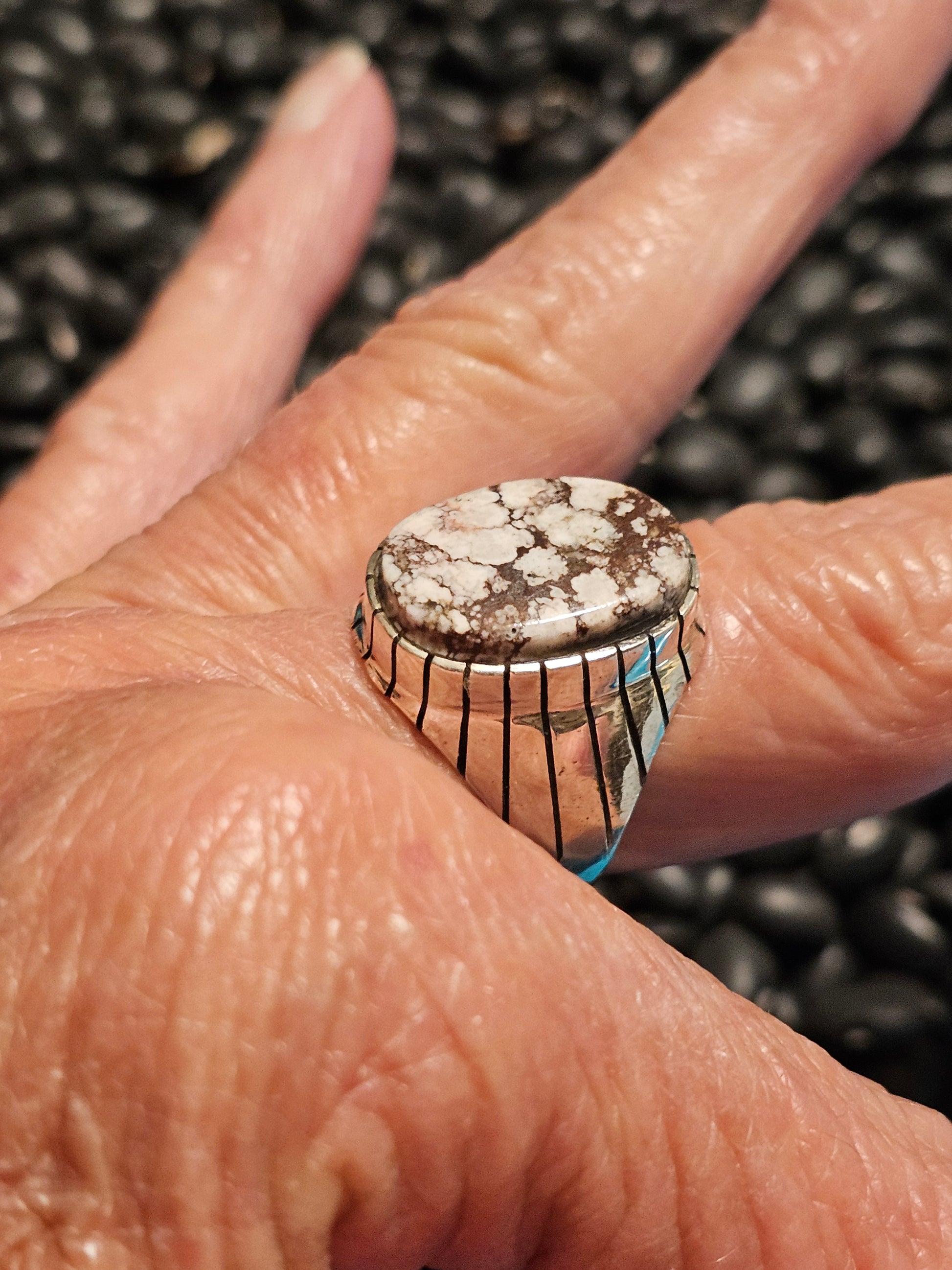 Close-up of a hand wearing a silver ring with a large stone on a textured background